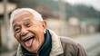 © RiadArt - Happy elderly man with flat cap making a funny face, sticking out tongue outdoors. Senior humor, joyful expression, active lifestyle, old age happiness concept.
