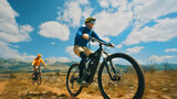 A thrilling close-up shot of two cyclists riding their e-bikes on a dirt trail, showcasing their off-road biking skills and the freedom of cycling in nature. The perspective emphasizes their speed.