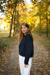 © Anhelina  - Young woman walking through an autumn park, looking back with a smile. Golden leaves cover the path, sunlight filtering through trees. Hair in motion adds energy and a joyful, carefree feel.