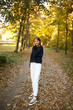 © Anhelina  - Young woman walking through an autumn park, looking back with a smile. Golden leaves cover the path, sunlight filtering through trees. Hair in motion adds energy and a joyful, carefree feel.