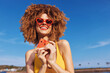 © SHOTPRIME STUDIO - Happy woman in heart shaped sunglasses holding a slice of watermelon at the beach under a clear blue sky