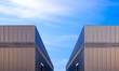 © Prapat - Two industrial warehouse factory buildings with ventilation louver on black corrugated metal wall against blue sky background, symmetric view with copy space
