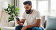 © Jonathan - Young bearded man paying online with smartphone on sofa at home. Customer makes secure purchase, uses mobile banking app. E-commerce, online shopping, fintech transaction concept.