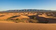 © Sya - Desert landscape with sand dunes under clear blue sky, mountain ridge in the distance