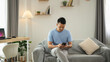 © WMSTUDIO - Young Man Sitting on Couch Using Smartphone in Modern Living Room with Cozy Decor and Neutral Color Palette