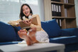 © Parichat - Young woman relaxing on sofa reading book and smiling