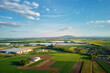 © Lazy_Bear - Aerial view of industrial warehouse complex near green agricultural fields and small village. Modern logistics infrastructure in rural landscape