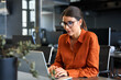 © Stock 4 You - European mature woman in eyeglasses using computer for finance data analysing work online. Focused financial specialist latin hispanic businesswoman working on laptop pc sitting at desk in office.
