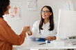 © Home-stock - Medical services concept. Cheerful woman doctor and female patient handshaking during meeting in clinic, therapist welcoming lady