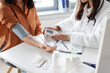 © Home-stock - Young lady examining female patient measuring arterial blood pressure with tonometer medical device, sitting at table. Hypertension health problem concept