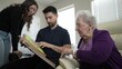 © Robert Peak - Family members gather at grandmother’s home, sharing stories and looking through a cherished photo album, creating lasting memories across generations.