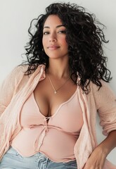 Wall Mural - a woman with long, curly hair wearing a pink cardigan and a pink top, standing in front of a white w