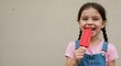 © Vyatcheslav - Smiling girl enjoying red ice pop while standing against a wall