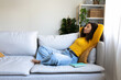 © Daniel - Side view of African American woman relaxing on the couch at home living room. Copy space.