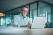 © ttonaorh - A smiling businessman working on a laptop in a modern office with natural lighting and soft colors, and a minimalistic office background.