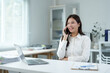 © crizzystudio - Businesswoman talking on phone and working on laptop in office