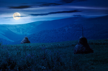 Wall Mural - rural mountain landscape in summer at night. haystack on green hill near village. alpine scenery at 