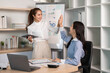 © wichayada - Celebrating Team Success. Two women high-fiving in a modern office after achieving goals.