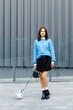© nazariykarkhut - Young woman walking her dog in the city wearing a blue sweater and black skirt