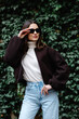 © nazariykarkhut - Fashionable woman adjusting sunglasses posing in front of ivy wall