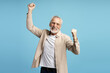 © Maria Vitkovska - Euphoric senior man celebrating success with raised fists on blue background