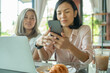 © sutlafk - two cheerful and beautiful girls are sitting together near the table and watching something on the phone. they look relaxed and happy. also girls are enjoying the time spending together.