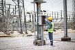 © JD Studio - Engineer is working attentively at high voltage substation wearing safety gear and yellow helmet while inspecting electrical equipment in industrial outdoor environment