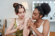 © Ekkasit A Siam - african female teen applies cream to asian female teen arm during skincare review recording while both concentrate and collaborate in cozy room with soft lighting and beauty tools