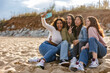 © PintoArt - Four young women taking a selfie on the beach, sticking out their tongues