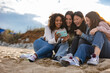 © PintoArt - Four young women laughing at smartphone content on the beach