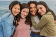 © PintoArt - Four young women embracing and smiling at the beach