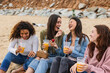 © PintoArt - Cheerful young women enjoying picnic on the beach, drinking juice and eating fruit