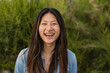 © PintoArt - Young woman laughing with green foliage background, expressing happiness outdoors