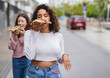 © PintoArt - Two happy women eating pizza slices while walking down the street