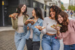 © PintoArt - Cheerful young women eating pizza slices and walking down the street