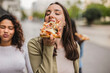 © PintoArt - Young women eating pizza outdoors in the city