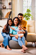 © StockImageFactory - Smiling Indian family sitting on floor near sofa, bonding together in stylish cozy living room