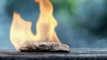 Aufkleber - Stone in Fire: A close-up shot of a rough, grey stone heating intensely in a vibrant flame, against a blurred natural background.