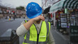 © Krakenimages.com - Young man in reflective vest and hardhat wiping sweat outdoors on city street, conveying fatigue and heat during a sunny day.