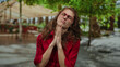 © Krakenimages.com - Woman wearing red glasses and shirt praying hopefully in a sunny park surrounded by green trees and blurred buildings.