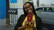 © Krakenimages.com - Woman smiling and holding a french passport at an outdoor petrol station with pumps and a car in the background, conveying travel readiness and diversity.