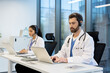 © Liubomir - A male and female doctors wearing headsets and lab coats, working on laptops in a modern office setting. Telemedicine concept.