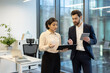 © Liubomir - Two business professionals, a woman and a man, are collaborating in a modern office setting, reviewing documents and using a tablet.