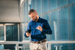 © Marko - Man checking phone while standing outside a modern building