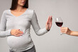 © Prostock-studio - No Alcohol. Unrecognizable Pregnant Lady Gesturing Stop To Offered Glass Of Wine Standing Over Gray Background. Studio Shot, Cropped