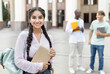 © Prostock-studio - Loans for education concept. Portrait of happy indian female student smiling at camera while posing outdoors in campus with her classmates and university building on background