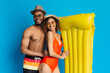 © Prostock-studio - Love water. Happy black loving couple embracing, going to beach with inflatable mattress, blue studio background