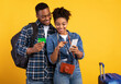 © Prostock-studio - Happy Black Couple Booking Travel Tickets Online Using Smartphone And Credit Card Standing With Suitcase Over Yellow Studio Background. Mobile Banking Abroad, Traveling Budget And Finances.