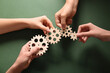 © Pixel-Shot - Hands holding wooden gears on green background, top view