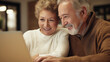 © Curioso.Photography - An elderly couple sitting together at home, smiling and looking at a laptop screen, representing modern technology in older age.